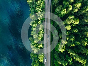 Aerial view of road between green tree forest and blue lake sea water in Finland