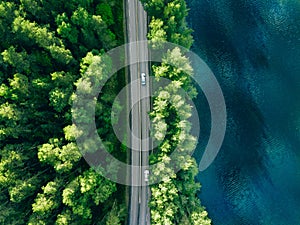 Aerial view of road between green tree forest and blue lake sea water in Finland