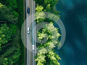 Aerial view of road between green tree forest and blue lake sea water in Finland