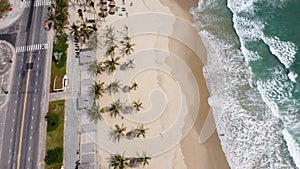 Aerial view of a road and majestic white sand beach with surf waves brushing on the seashore on a sunny day.