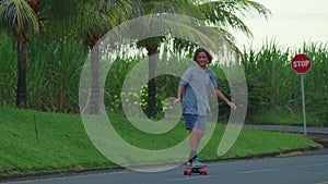 Aerial view of the road with palm trees. Boy riding a skateboard on a beautiful road. Teenager skateboarding on city