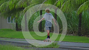 Aerial view of the road with palm trees. Boy riding a skateboard on a beautiful road. Teenager skateboarding on city