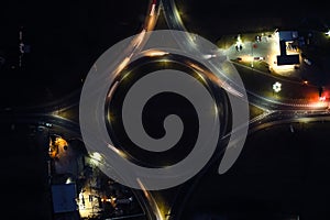 Aerial view of road roundabout intersection with fast moving heavy traffic at night. Top view of urban circular