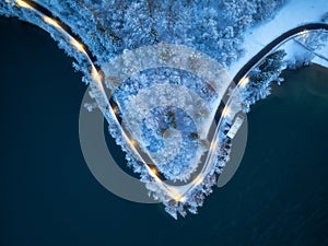 Aerial view of road, snowy forest, lake, street lights at night