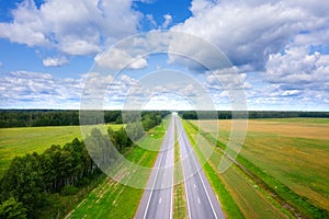 Aerial view of road on sunny summer day. Empty Highway from above. Beautiful landscape of road between green meadow and blue sky