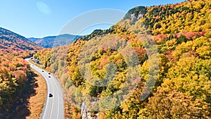 Aerial view of road tucked into New Hampshire mountains covered in peak fall foliage