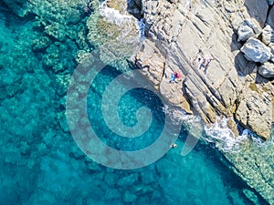 Aerial view of rocks on the sea. Swimmers, bathers floating on the water. eople sunbathing on the towel