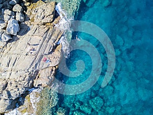 Aerial view of rocks on the sea. Swimmers, bathers floating on the water. People sunbathing on the towel