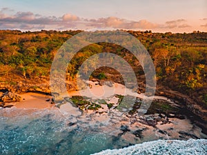 Aerial view of rocky coastline with beach, waves and warm light. Bali, Indonesia