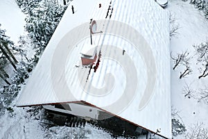 Aerial view of the roof of a family house with a chimney and a satellite dish in the forest after heavy snowfall in winter