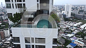 Aerial View Of Rooftop Swimming Pool In Bangkok, Thailand With Digital Nomad Sitting And Using Smartphone By The