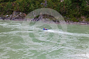Aerial view of a rubber motor boat sailing on a green river in the mountains between rocks and cliff