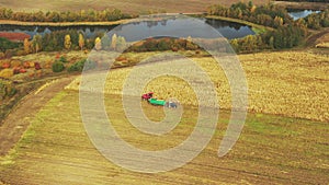 Aerial View Of Rural Landscape. Combine Harvester And Tractor Working In Corn Field. Collects Dry Corn Plants