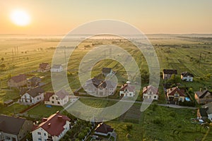 Aerial view of rural residential area with private homes between green fields at sunrise