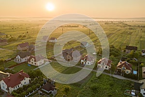 Aerial view of rural residential area with private homes between green fields at sunrise