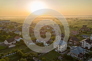 Aerial view of rural residential area with private homes between green fields at sunrise