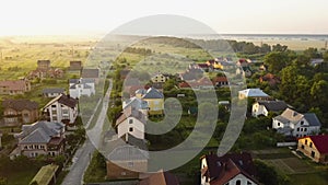 Aerial view of rural residential area with private homes between green fields at sunrise.