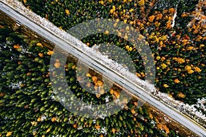 Aerial view of rural road with first snow in yellow and orange autumn forest