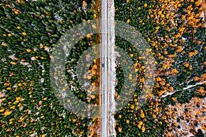 Aerial view of rural road with first snow in yellow and orange autumn forest