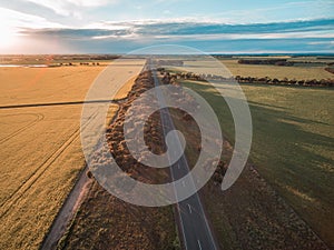 Aerial view of rural road passing through agricultural land in Australian countryside at sunset.