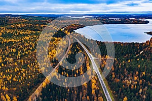 Aerial view of rural road with red car in yellow and orange autumn forest with blue lake