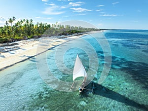 Aerial view of the sailboat on blue sea, empty white sandy beach