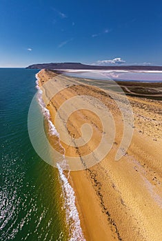 Aerial view of sand spit between clear azure sea and pink lake with salt