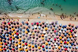 Aerial view of sandy beach with colorful umbrellas, swimming people in sea bay with transparent blue water in summer