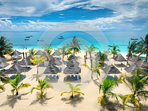 Aerial view of sandy beach with palm trees, umbrellas, boats, sea