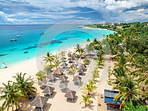 Aerial view of sandy beach with palm trees, umbrellas, boats, sea