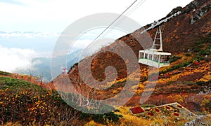 Aerial view of a scenic cable car gliding over the clouds up to the autumn mountains in Japanese Central Alps National Park, Ngano