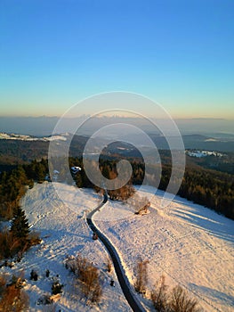Aerial view of a scenic winter landscape with a winding road surrounded by trees