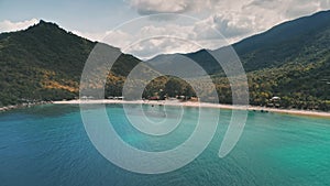 Aerial view, sea coast island with mountains and forest. Grey clouds over azure ocean water.