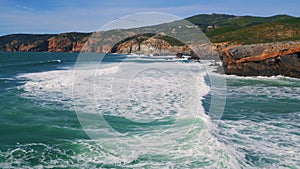 Aerial view sea waves barreling to rocky shoreline with white foam slow motion