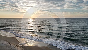 Aerial view of sea waves breaking sandy beach during sunset