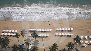Aerial view of sea waves, umbrellas, green palms on the sandy beach. Tropical landscape. Top view from air. Nha trang