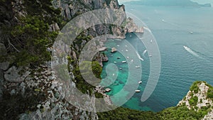 Aerial view of seascape with boats and dramatic rocky cliffs against blue waters of sea. Capri Island in summertime.