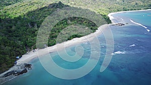 An aerial view of a secluded beach with powdery white sand, turquoise water, and a lush green forest lining the shore.