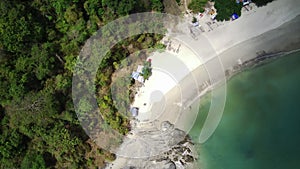 An aerial view of a secluded beach with powdery white sand, turquoise water, and a lush green forest lining the shore.