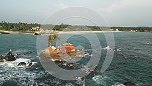 Aerial view of secluded island house among ocean waves near coast. Exclusive retreat for getaway, honeymoon, solitude