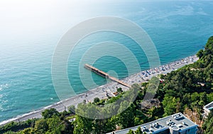 Aerial view of serene beach with long pier, azure waters, and vibrant beachgoers dotting shoreline