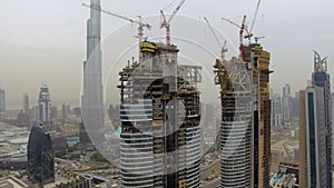 Aerial view of several skyscrapers under construction with scaffolding and cranes. Dubai, UAE