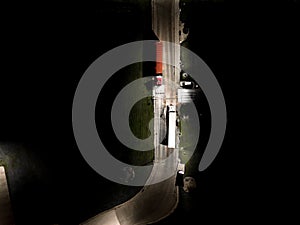 Aerial view of a sharp turn on a mountain road among green forest trees. Semi truck with cargo trailer and bright headlights on a