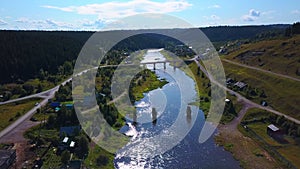 Aerial view of a shiny river and a village surrounded by green vegetation. Clip. Summer natural landscape.