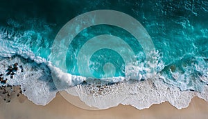 Aerial view of turquoise ocean waves crashing on a sandy beach with rocks on the left side of the shore