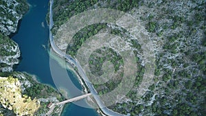 The aerial view shows a winding road snaking through the rugged mountains, surrounded by lush greenery and rocky terrain