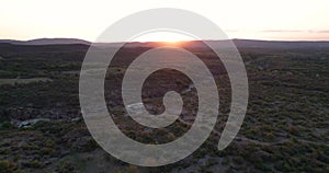 Aerial view of the sierras in the background with the sun setting on them.