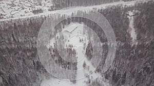 Aerial view of a single-family house in the forest during the winter with lots of snow in the forest and on the roof