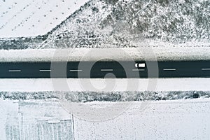 Aerial view of single white car on the road through frozen countryside landscape covered in snow