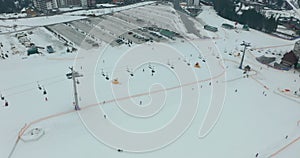 Aerial view: ski resort, slope and chair lift. Cableway lifts skiers to the mountain hill. Winter activity.